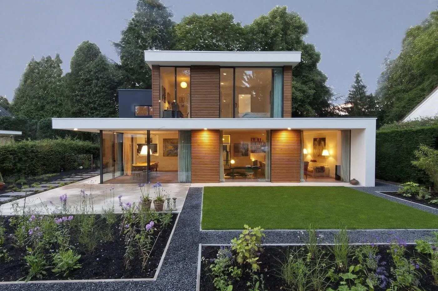 Villa met witte bovenbouw, houten gevel en glas van vloer tot plafond, 's avonds verlicht
