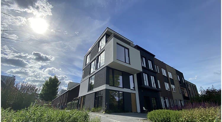 Blok met woningen van drie lagen, donkere gevel, in de ochtendzon