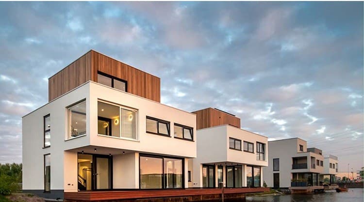 Zes opgeleverde woningen in staalframe met witte en houten volumes aan een kade